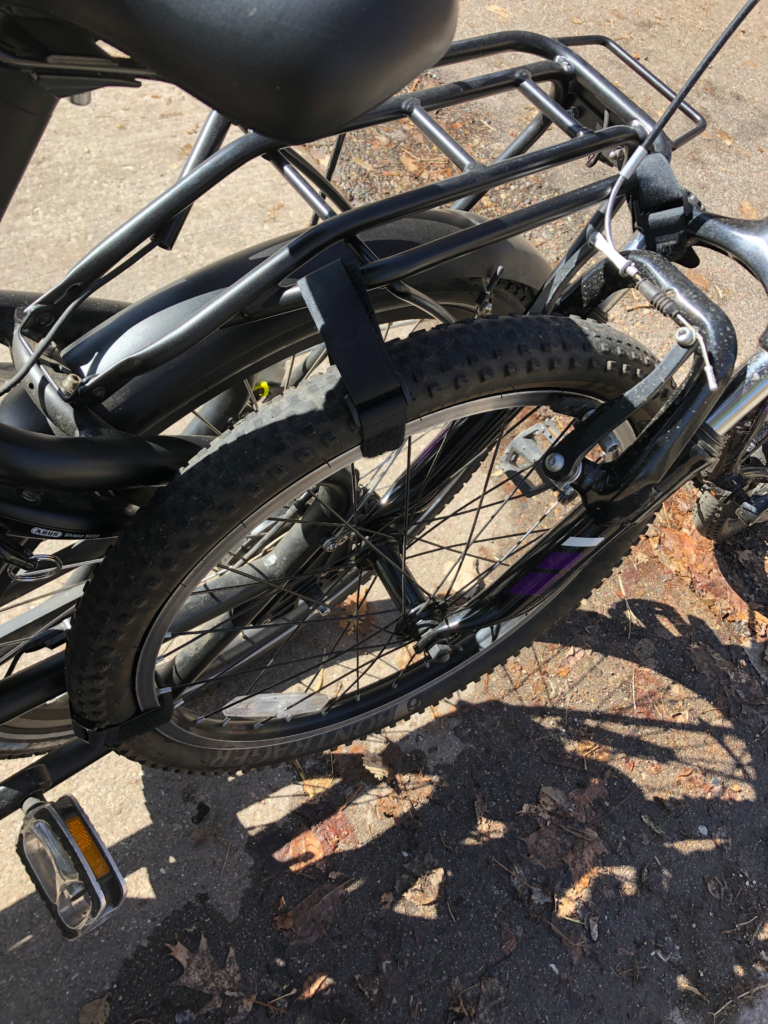 a child's bike wheel attached to the rear luggage rack of a bakfiets style cargo bike with black velcro straps.